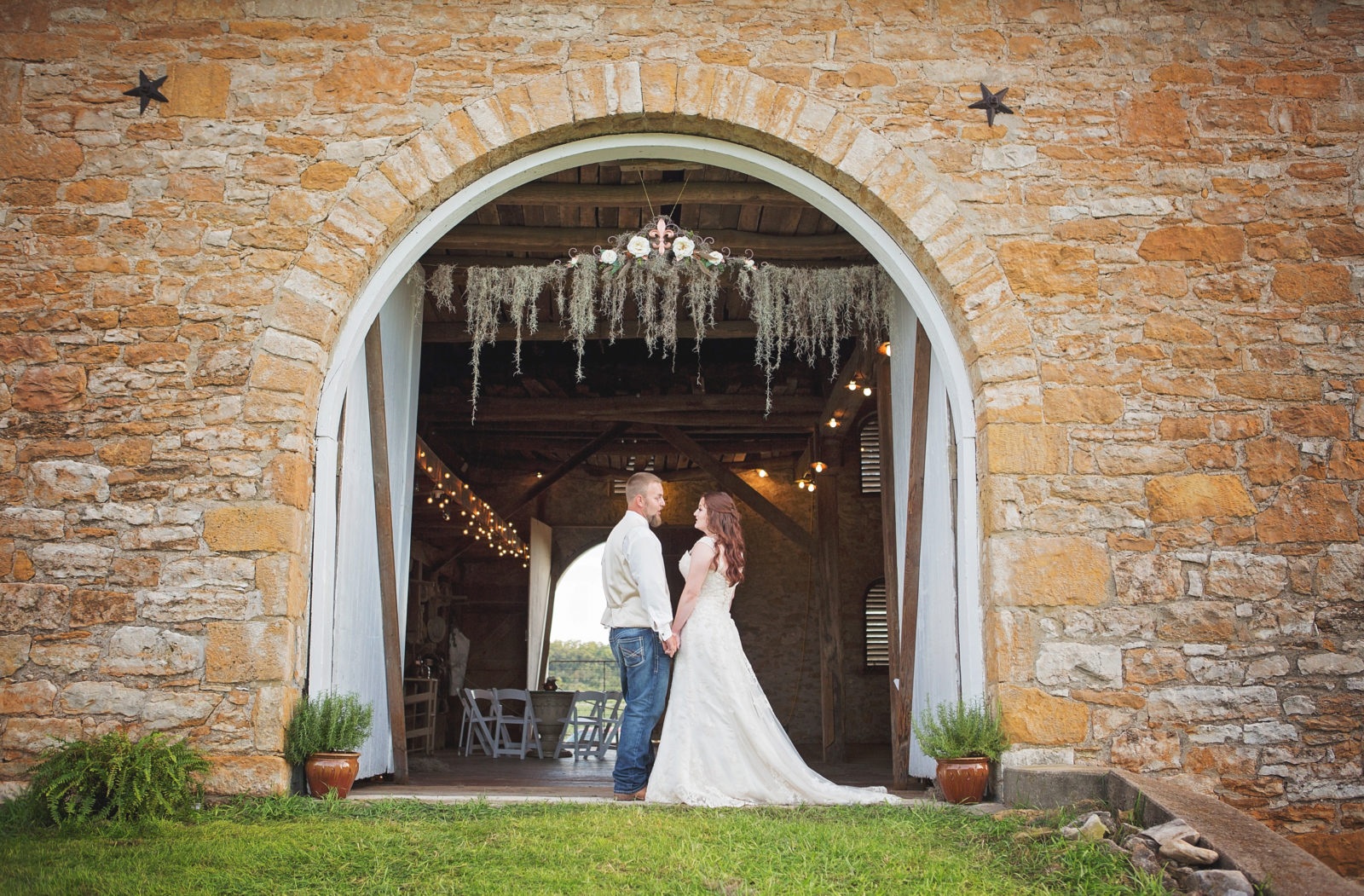 Bride and groom share a kiss under a rustic archway.