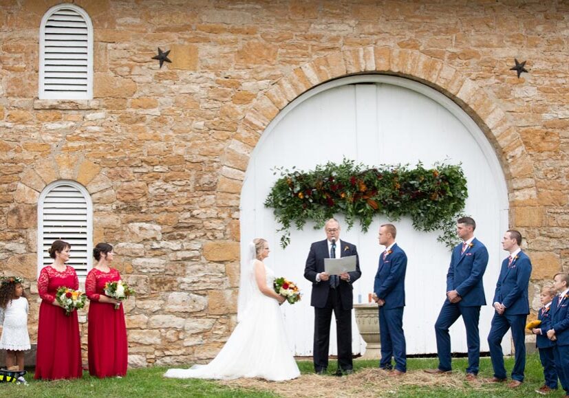 Outdoor wedding ceremony by rustic stone building.